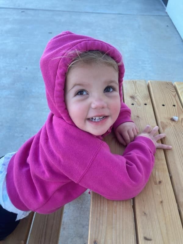 A young child in a pink jacket smiling in Funshine's outdoor play area