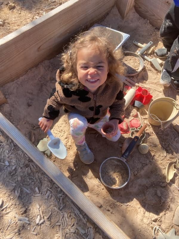 A child smiling while exploring the outdoor mud kitchen at Funshine